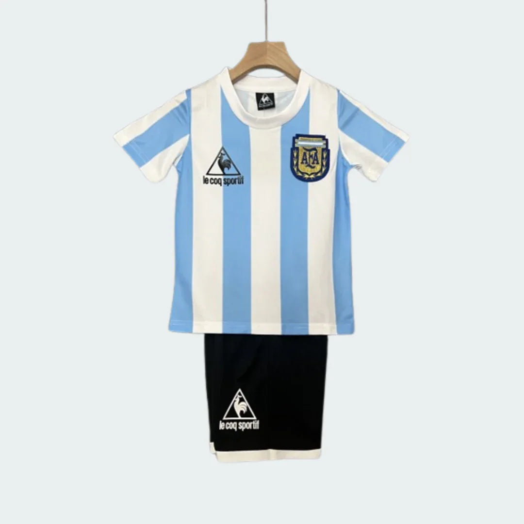 Kit infantil da Argentina com a tradicional camisa listrada em azul claro e branco, três estrelas acima do escudo e calção preto.