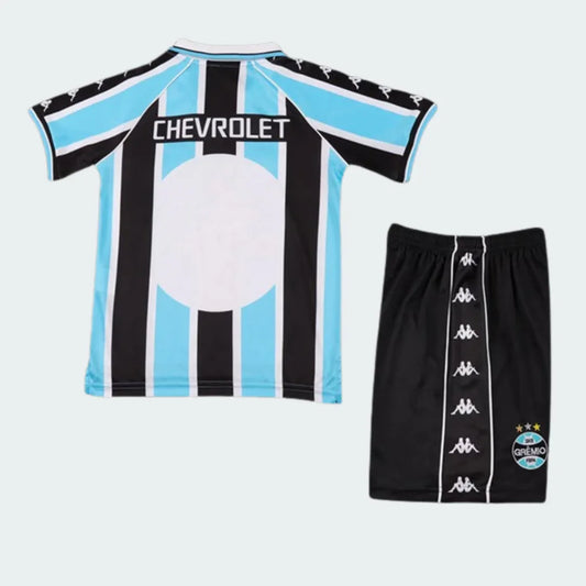 Kit infantil de futebol do Grêmio, camisa listrada preta e azul claro com shorts preto. Estampa Chevrolet na camisa e logo Kappa nas mangas e shorts.