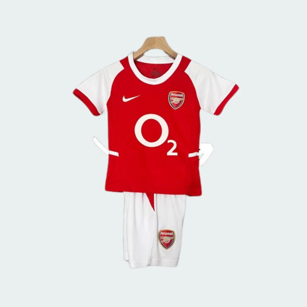 Kit infantil retrô Arsenal, camisa vermelha com mangas brancas e shorts brancos, logo O2. Escudo do Arsenal na camisa e shorts.
