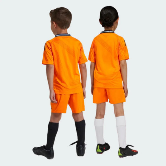 Dois jovens atletas, de costas, vestindo kits de futebol laranja com gola azul-marinho e detalhes de listras diagonais.