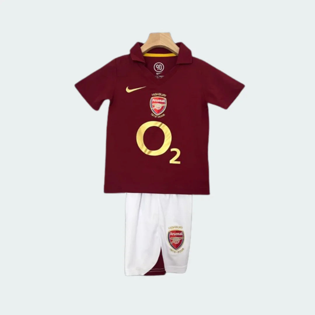 Kit infantil retrô Arsenal: camisa polo bordô com detalhes dourados Nike, O2 e escudo do time. Shorts brancos com escudo.
