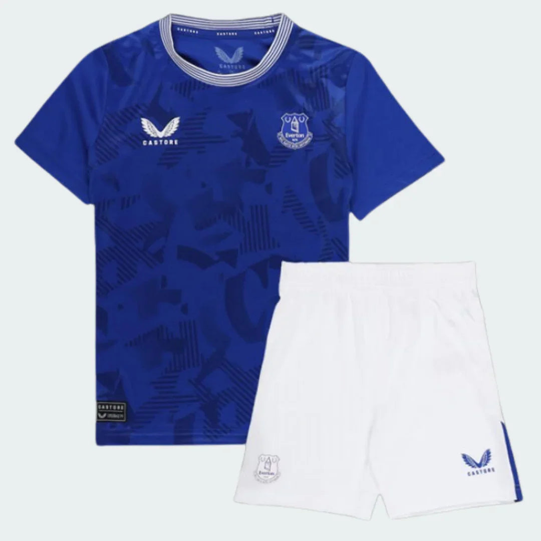 Kit infantil Everton I 24/25. Camisa azul principal com estampa geométrica sutil e shorts brancos. Escudo Everton e logo Castore.