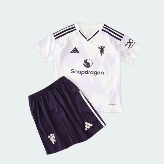 Kit infantil Manchester United branco e roxo escuro. Camisa branca com escudo, logo Adidas e Snapdragon pretos. Shorts roxo escuro com escudo e logo Adidas brancos.