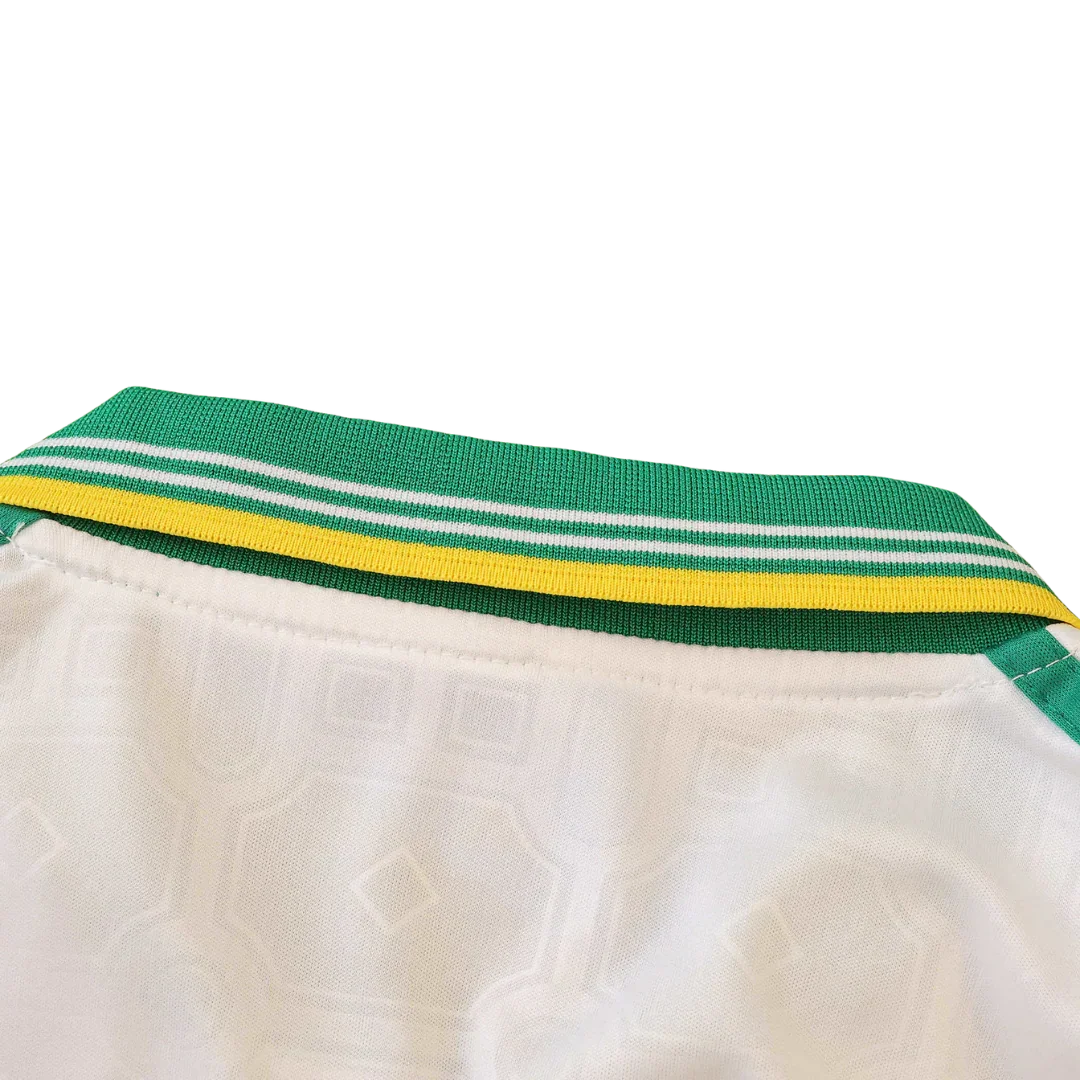 Detalhe da gola e parte superior de uma camisa de futebol infantil branca, com gola listrada em verde, branco e amarelo.