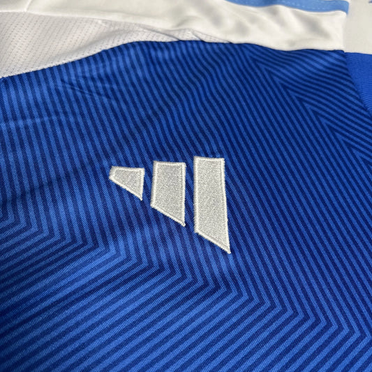 Camisa de futebol infantil azul com padrão listrado diagonal em tons de azul e detalhes brancos. Logo de três barras brancas bordado.