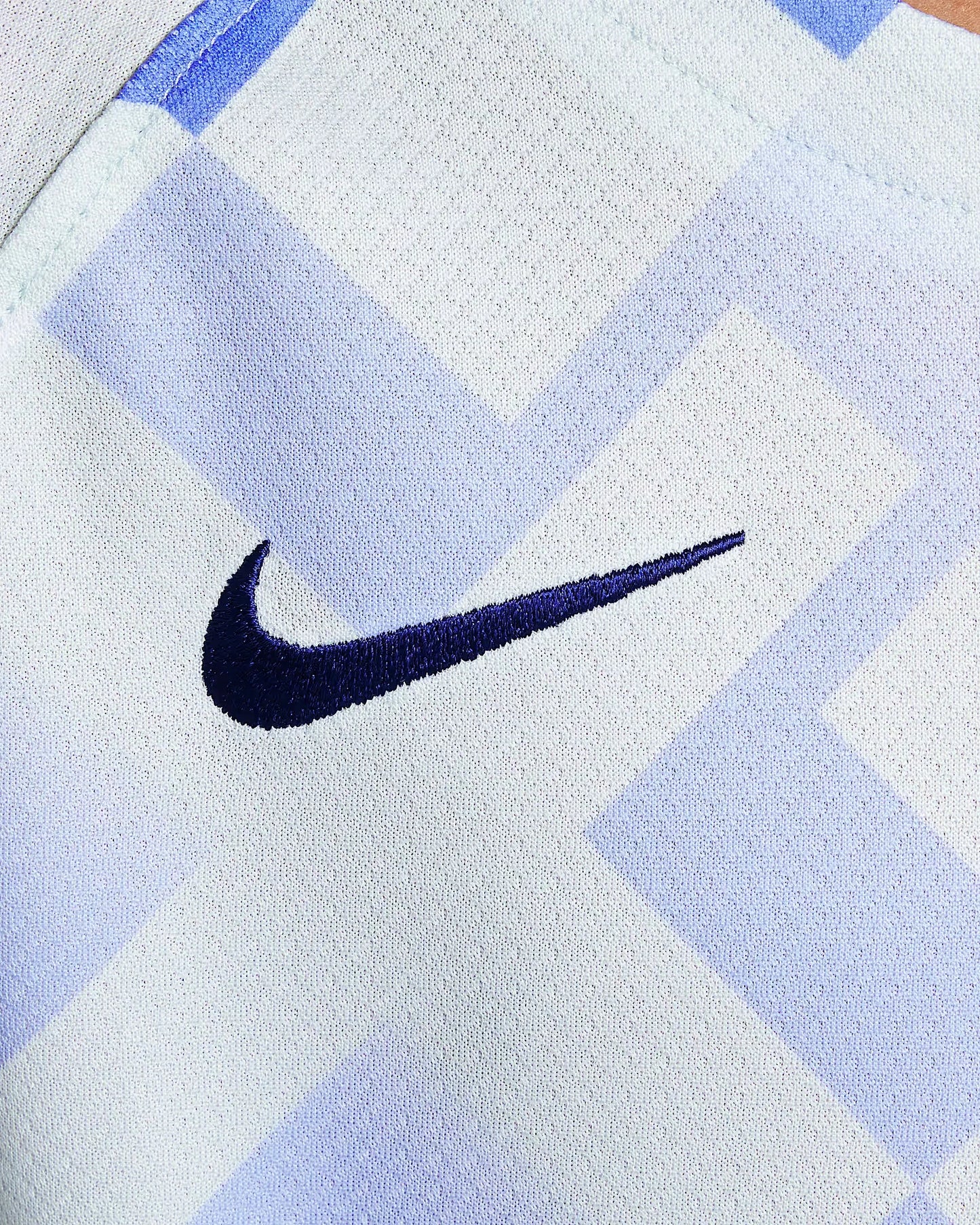 Close-up de tecido de camisa branco com padrão geométrico azul claro e logo Nike bordado em azul escuro.