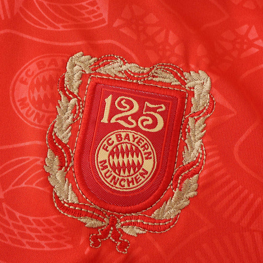 Escudo comemorativo de 125 anos do FC Bayern München bordado em dourado e vermelho sobre tecido de camisa vermelha.