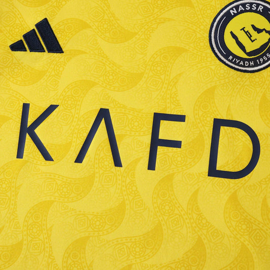 Kit oficial infantil Mini Mantos Al Nassr, camisa amarela KAFD, logo Adidas e distintivo do clube