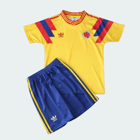 Kit infantil retrô da Colômbia 1990: camisa amarela com listras vermelhas/azuis e escudo, shorts azuis com listras amarelas e logo Adidas.