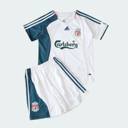Kit infantil Liverpool retrô 2006, camisa e shorts brancos com detalhes em verde petróleo, listras brancas e escudo.