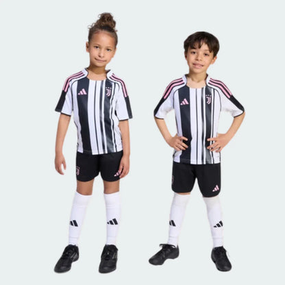 Duas crianças, uma menina e um menino, vestindo o kit infantil Juventus I, com camisa listrada em preto e branco, detalhes em rosa e calção preto.
