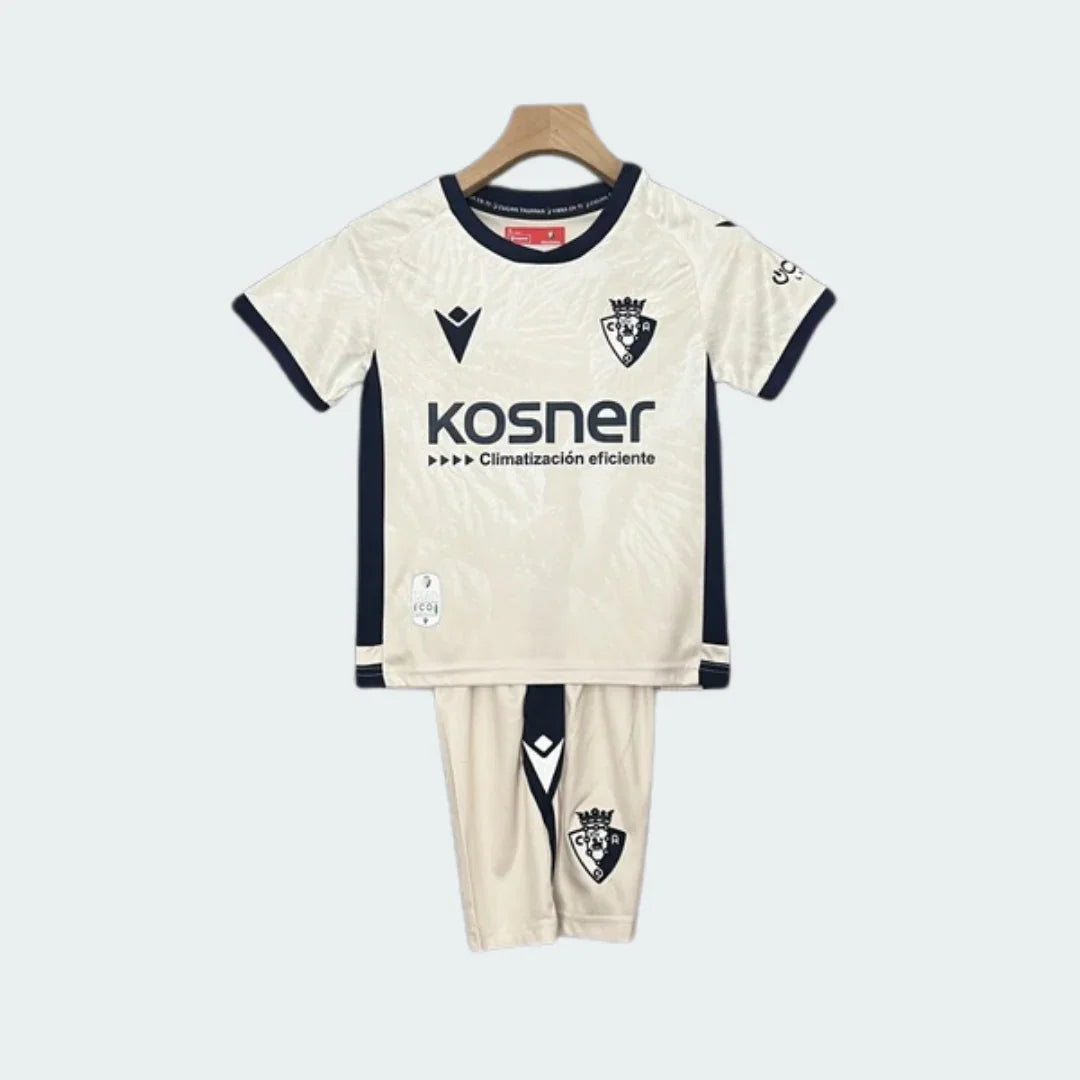 Kit infantil Osasuna II 24/25, com camisa e shorts off-white e detalhes azul-marinho, pendurado em cabide.