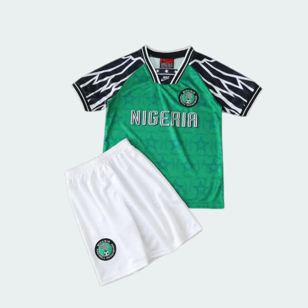 Kit infantil retrô Nigéria 94/95. Camisa verde com estampa de estrelas, gola V preta, mangas com listras brancas e pretas, e shorts brancos com escudo.
