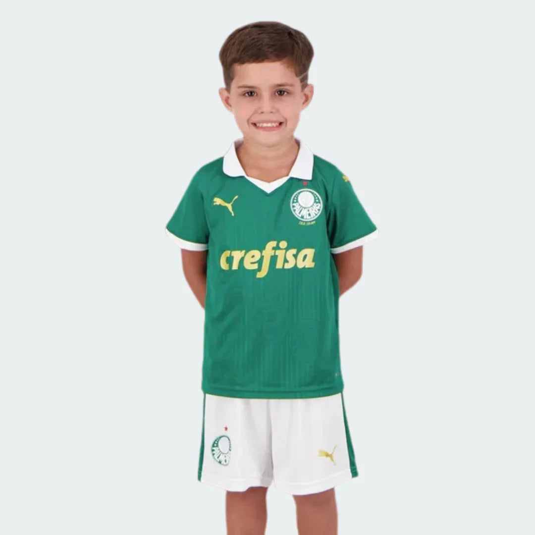 Menino sorridente veste kit de futebol infantil Verdão verde e branco. Camisa com logo Puma e Crefisa, shorts brancos.