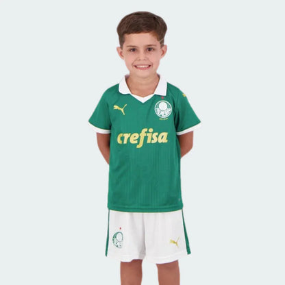 Menino sorridente veste kit de futebol infantil Verdão verde e branco. Camisa com logo Puma e Crefisa, shorts brancos.