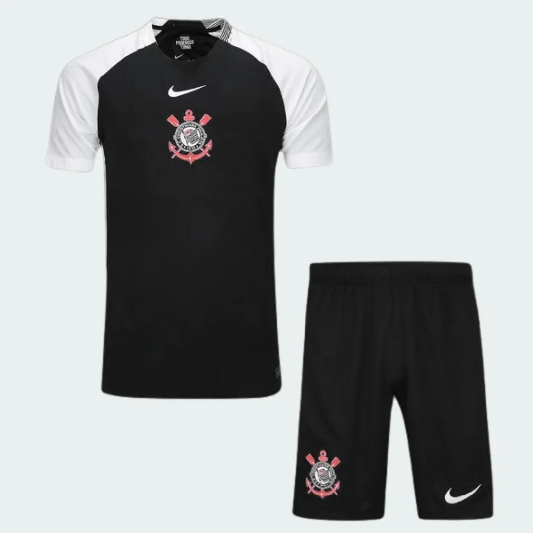Kit infantil do Timão 25/26, camiseta preta com mangas brancas e shorts pretos. Escudo do Corinthians e logo Nike em branco.