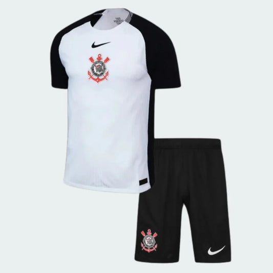 Kit infantil Timão I 25/26, camisa branca e preta com escudo e logo Nike, shorts pretos com escudo e logo Nike.