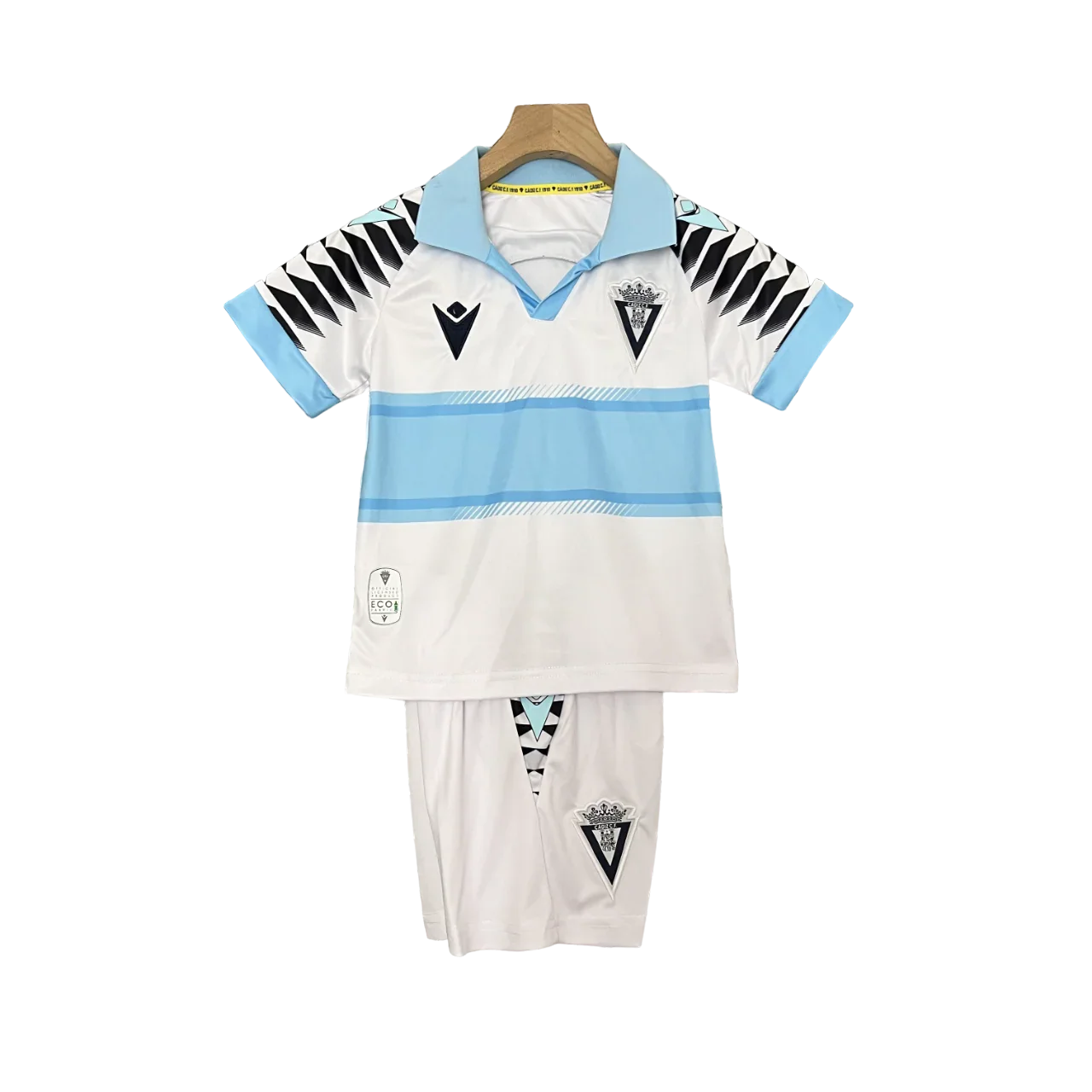 Kit infantil do Cádiz 24/25 (camisa e shorts) em branco com listras azuis claras, escudos do clube e Macron, pendurado.