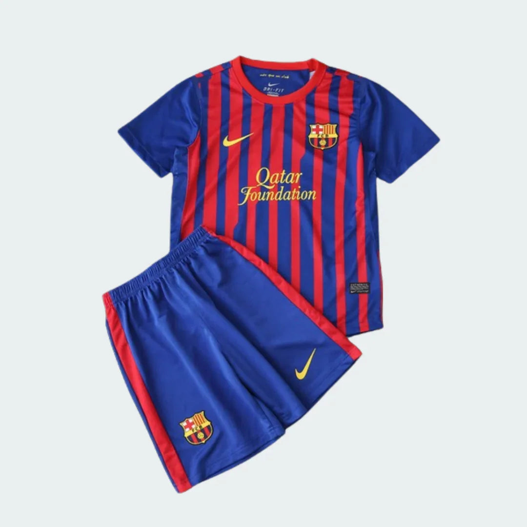 Kit infantil do Barcelona com camisa listrada em azul e vermelho e shorts azul. Camisa com escudo do Barcelona, Nike e 'Qatar Foundation'. Shorts com escudo do Barcelona e Nike.