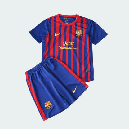 Kit infantil do Barcelona com camisa listrada em azul e vermelho e shorts azul. Camisa com escudo do Barcelona, Nike e 'Qatar Foundation'. Shorts com escudo do Barcelona e Nike.
