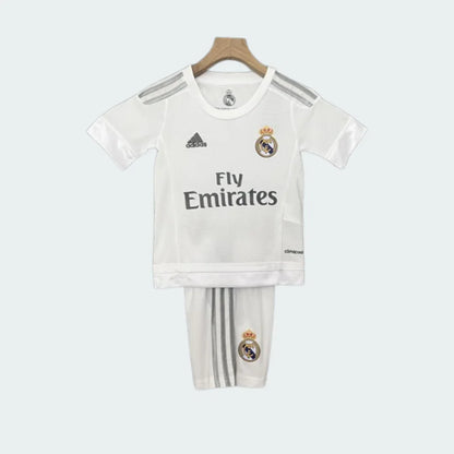 Foto de kit infantil retrô Real Madrid I 11/12 branco pendurado, com camisa e shorts. Detalhes em cinza e escudo.