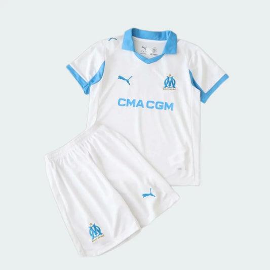 Foto de um kit infantil Olympique De Marseille branco e azul, incluindo camisa polo de manga curta e shorts. Logos Puma, CMA CGM e escudo do clube visíveis.