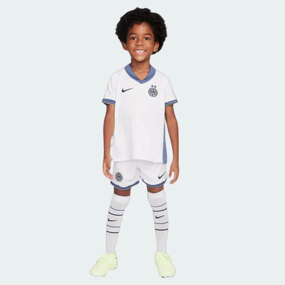 Criança sorrindo com kit infantil Inter de Milão II 24/25 branco, shorts e meiões. Escudo e logo Nike visíveis.