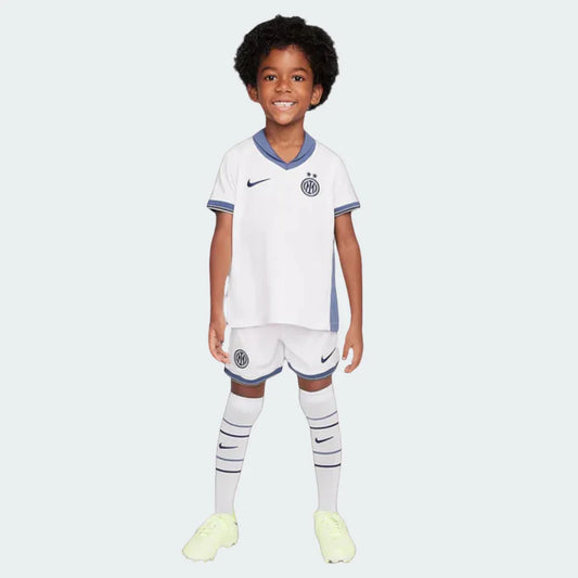 Criança sorrindo com kit infantil Inter de Milão II 24/25 branco, shorts e meiões. Escudo e logo Nike visíveis.