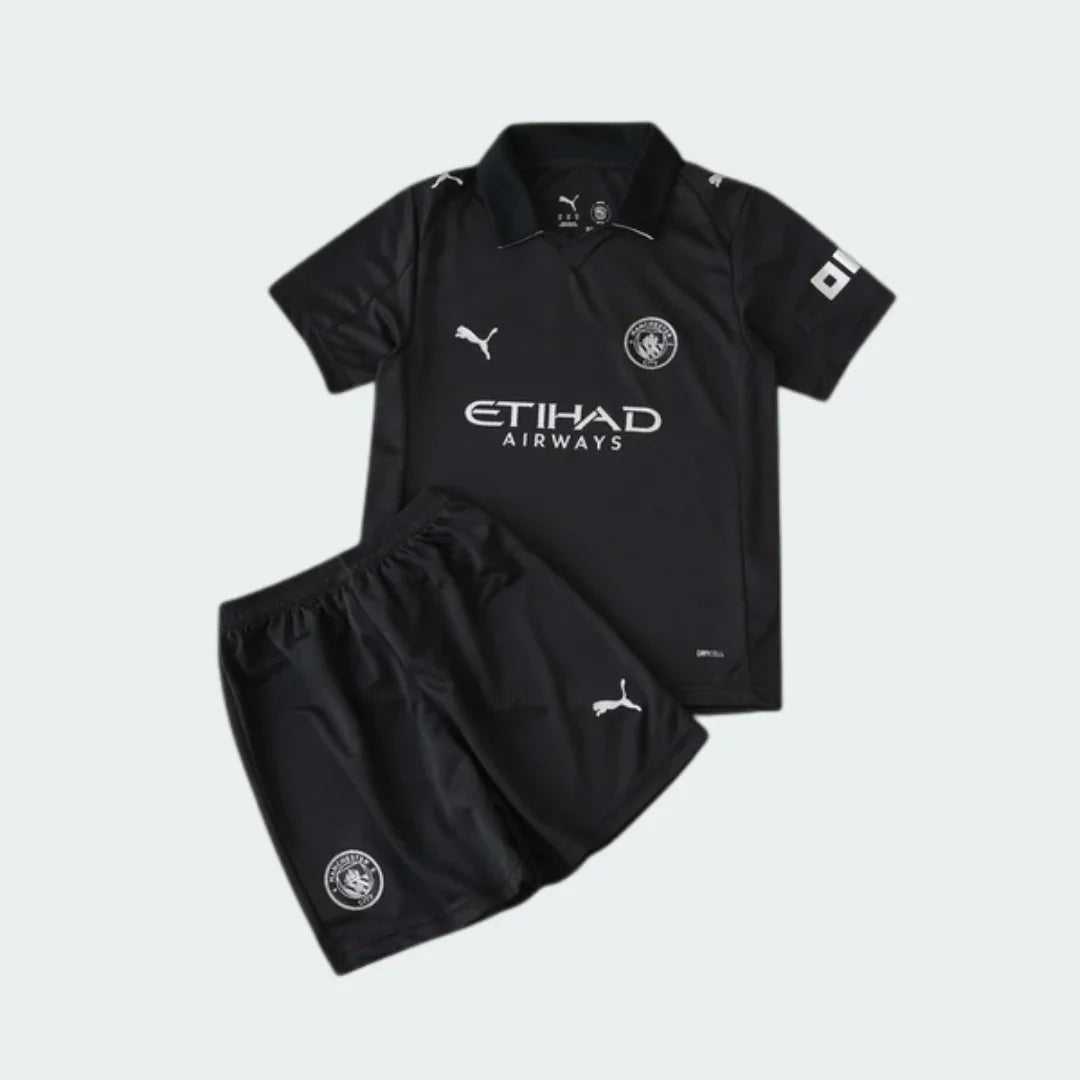 Kit infantil completo do Manchester City 25/26, camisa e shorts pretos. Logos Puma, escudo e Etihad Airways em branco.