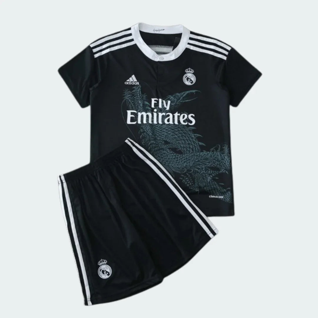 Kit infantil preto do Real Madrid com dragão, camisa e shorts. Escudo e logos Adidas e Fly Emirates brancos.