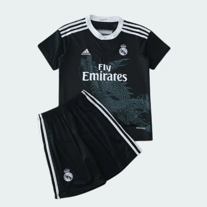 Kit infantil preto do Real Madrid com dragão, camisa e shorts. Escudo e logos Adidas e Fly Emirates brancos.