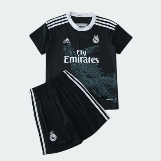 Kit infantil preto do Real Madrid com dragão, camisa e shorts. Escudo e logos Adidas e Fly Emirates brancos.