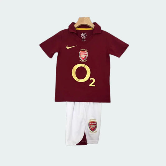 Kit infantil retrô Arsenal: camisa polo bordô com detalhes dourados Nike, O2 e escudo do time. Shorts brancos com escudo.