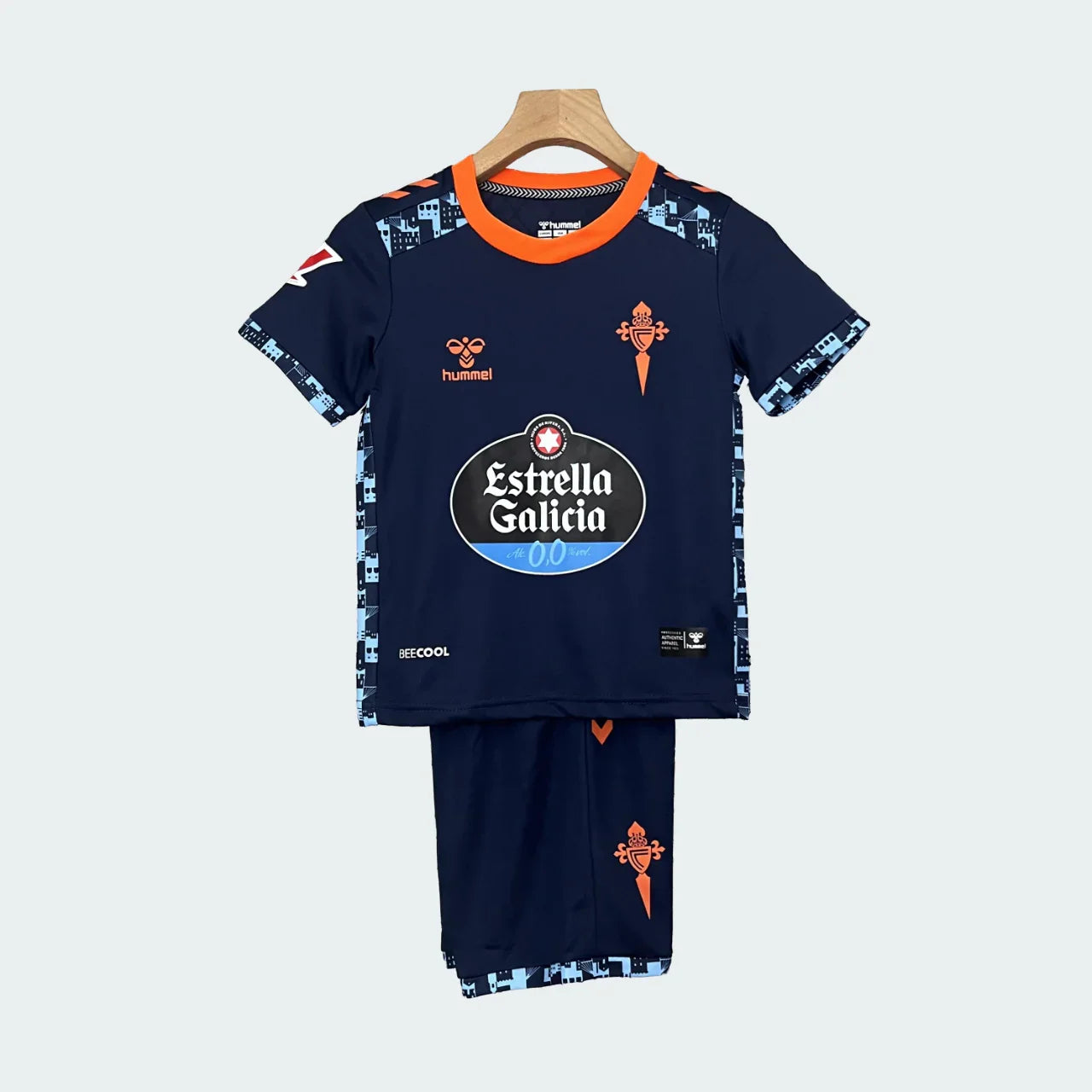 Kit infantil Celta Vigo II 24/25, camisa e shorts azul marinho com detalhes em laranja e azul claro, pendurado em cabide.