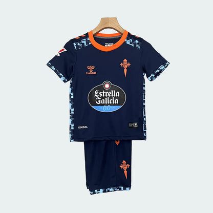 Kit infantil Celta Vigo II 24/25, camisa e shorts azul marinho com detalhes em laranja e azul claro, pendurado em cabide.