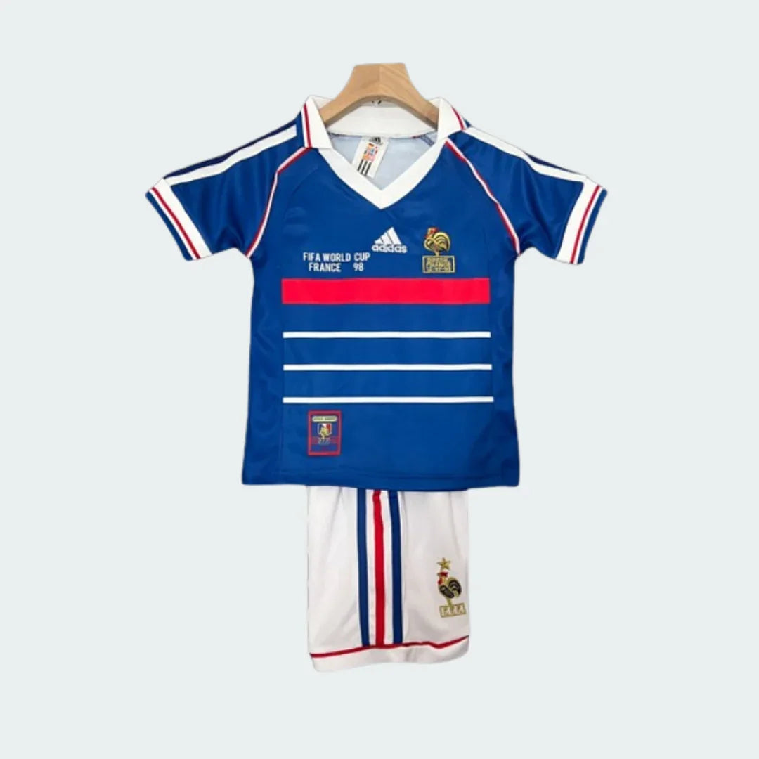 Kit infantil de futebol retrô Francia 1998. Camisa azul com listras e detalhes vermelhos e brancos, shorts brancos.