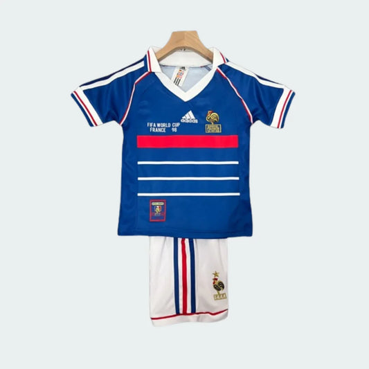Kit infantil de futebol retrô Francia 1998. Camisa azul com listras e detalhes vermelhos e brancos, shorts brancos.