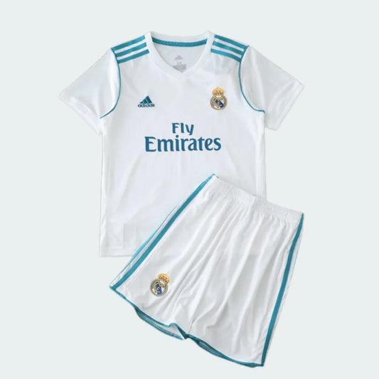 Kit infantil branco do Real Madrid com camisa e shorts. Detalhes em azul-turquesa, escudo do clube e patrocínio Fly Emirates.
