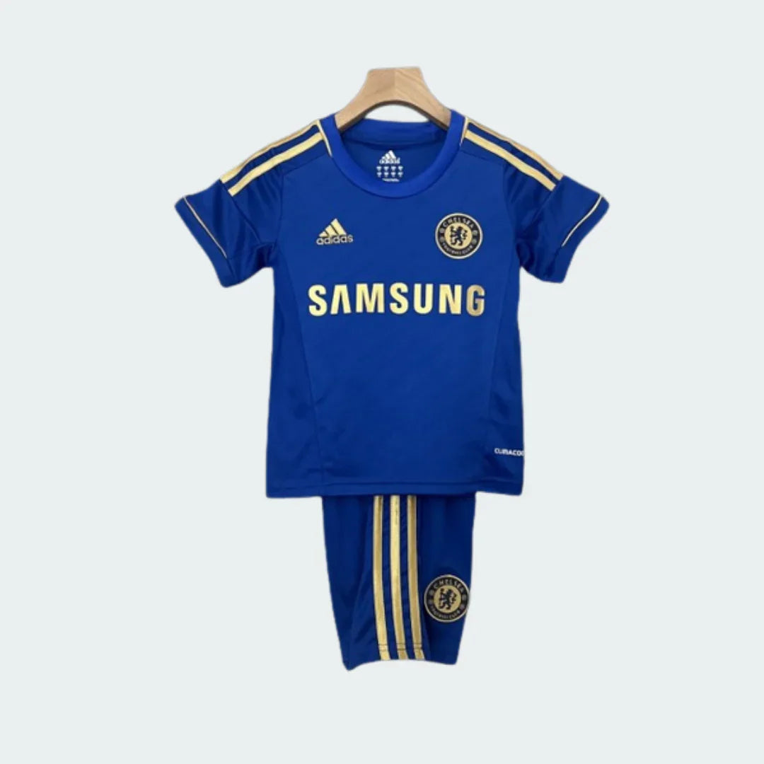 Kit de futebol infantil do Chelsea, camisa e shorts azuis com listras e detalhes dourados, logos Adidas, Samsung e escudo.