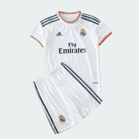 Kit infantil branco do Real Madrid com camisa e shorts. Camisa com listras cinzas nos ombros, escudo, Adidas e Fly Emirates. Shorts com listras e escudo.