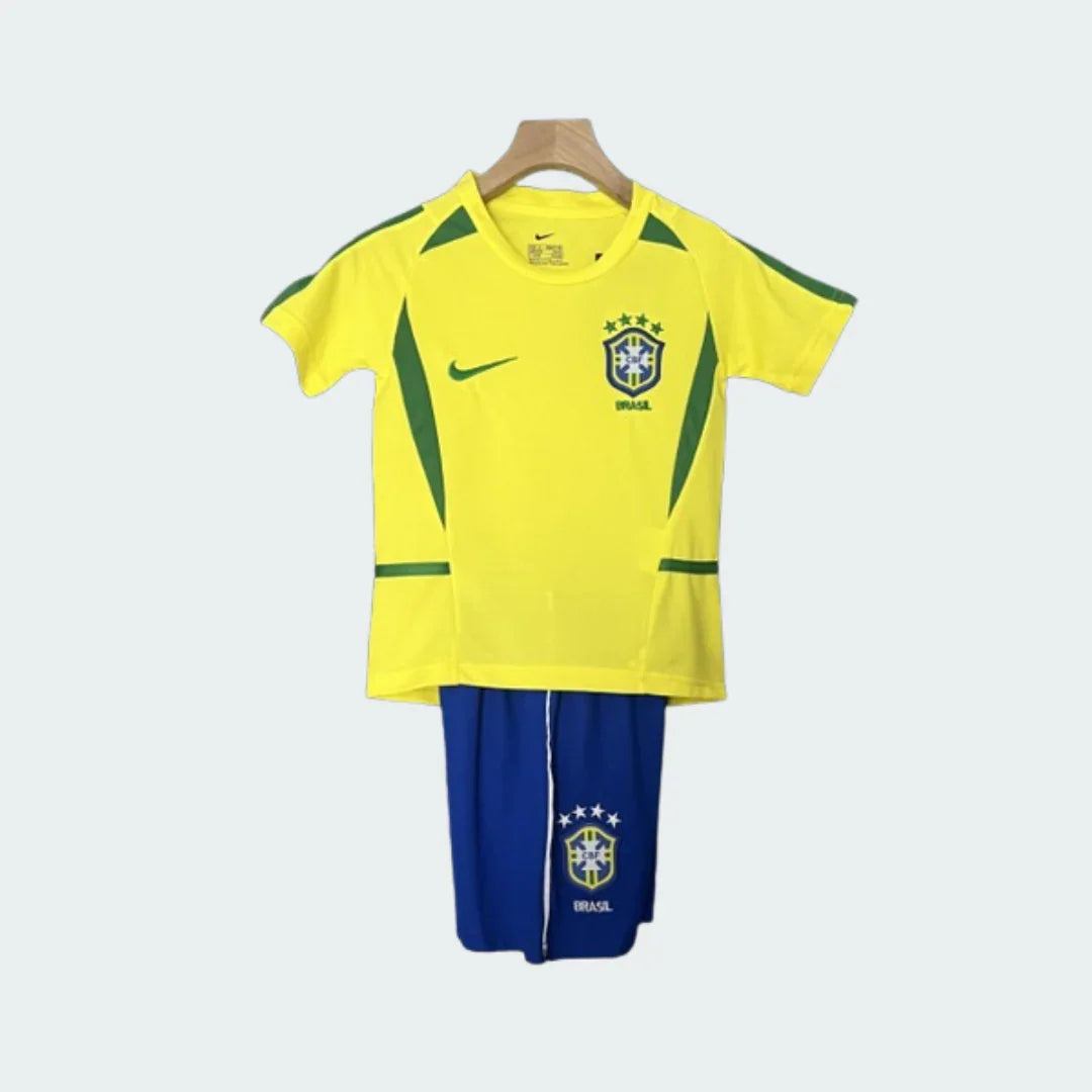 Kit infantil retrô Brasil I 2002 pendurado, composto por camisa amarela com detalhes verdes, escudo do Brasil e shorts azuis.