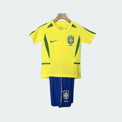 Kit infantil retrô Brasil I 2002 pendurado, composto por camisa amarela com detalhes verdes, escudo do Brasil e shorts azuis.