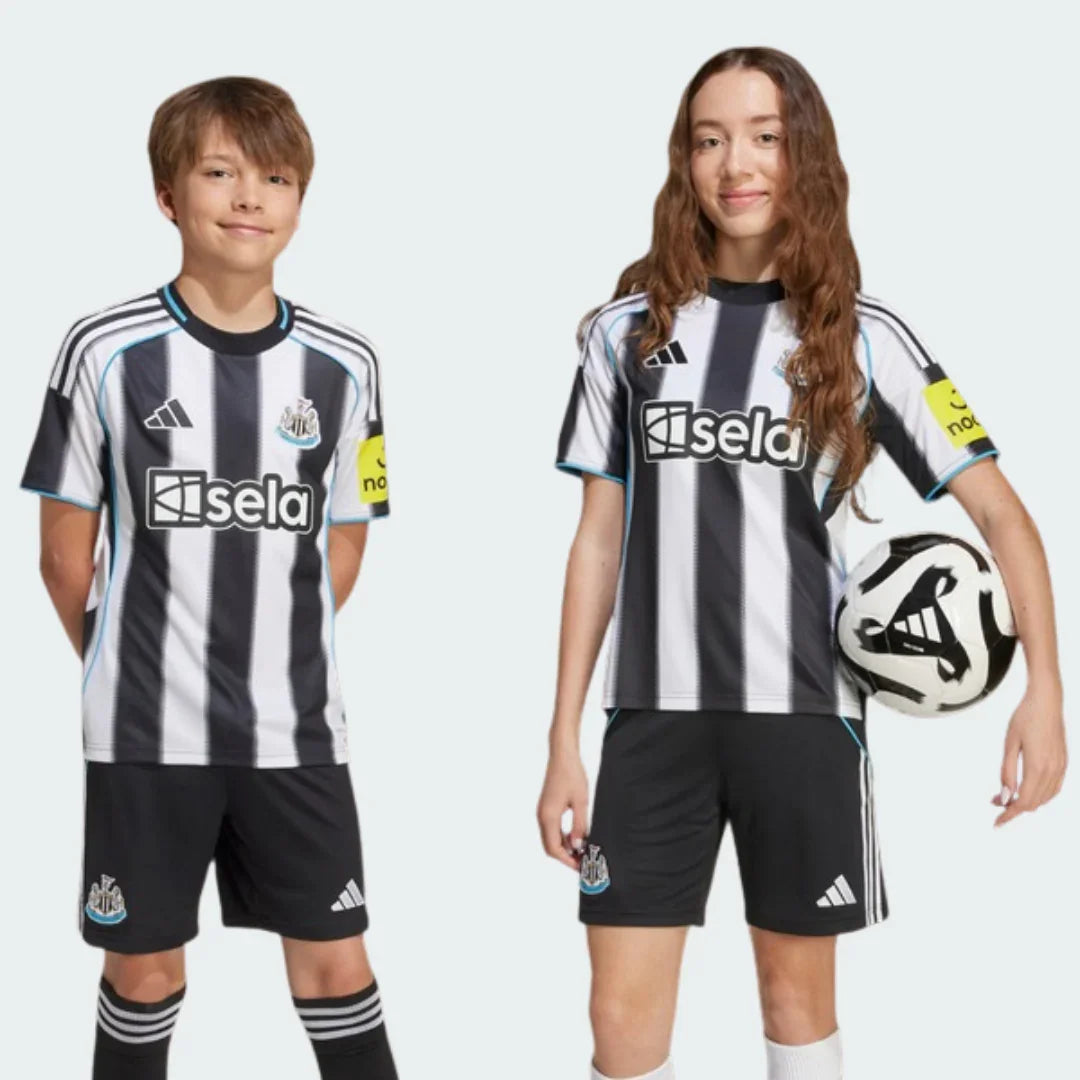 Duas crianças posam com o Kit Infantil Newcastle I 25/26. Camisa listrada preta e branca com detalhes azuis, shorts pretos, meias.