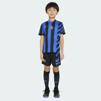 Menino sorridente em pé, vestindo o Kit Infantil Inter de Milão I 24/25. Camisa listrada azul e preta, shorts pretos e meias pretas.