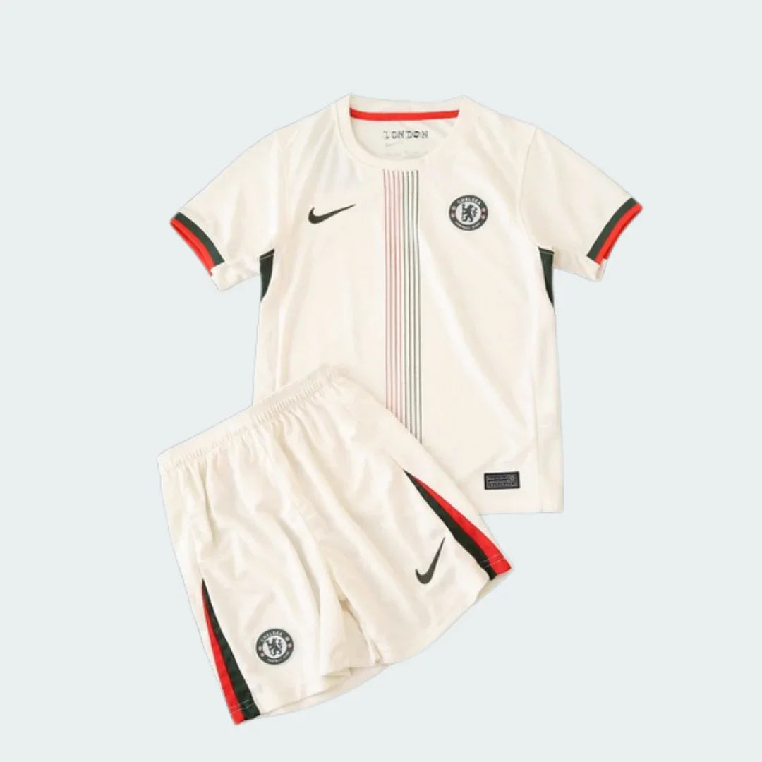 Kit infantil Chelsea II 25/26 com camisa e shorts creme. Detalhes em preto e vermelho, listras verticais na camisa, logos Nike e escudo.
