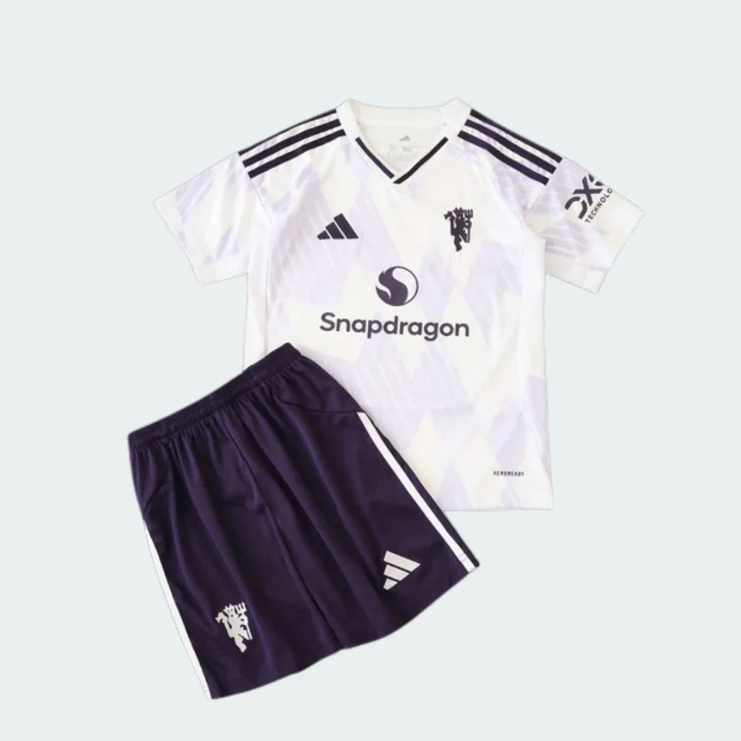 Kit infantil Manchester United branco e roxo escuro. Camisa branca com escudo, logo Adidas e Snapdragon pretos. Shorts roxo escuro com escudo e logo Adidas brancos.
