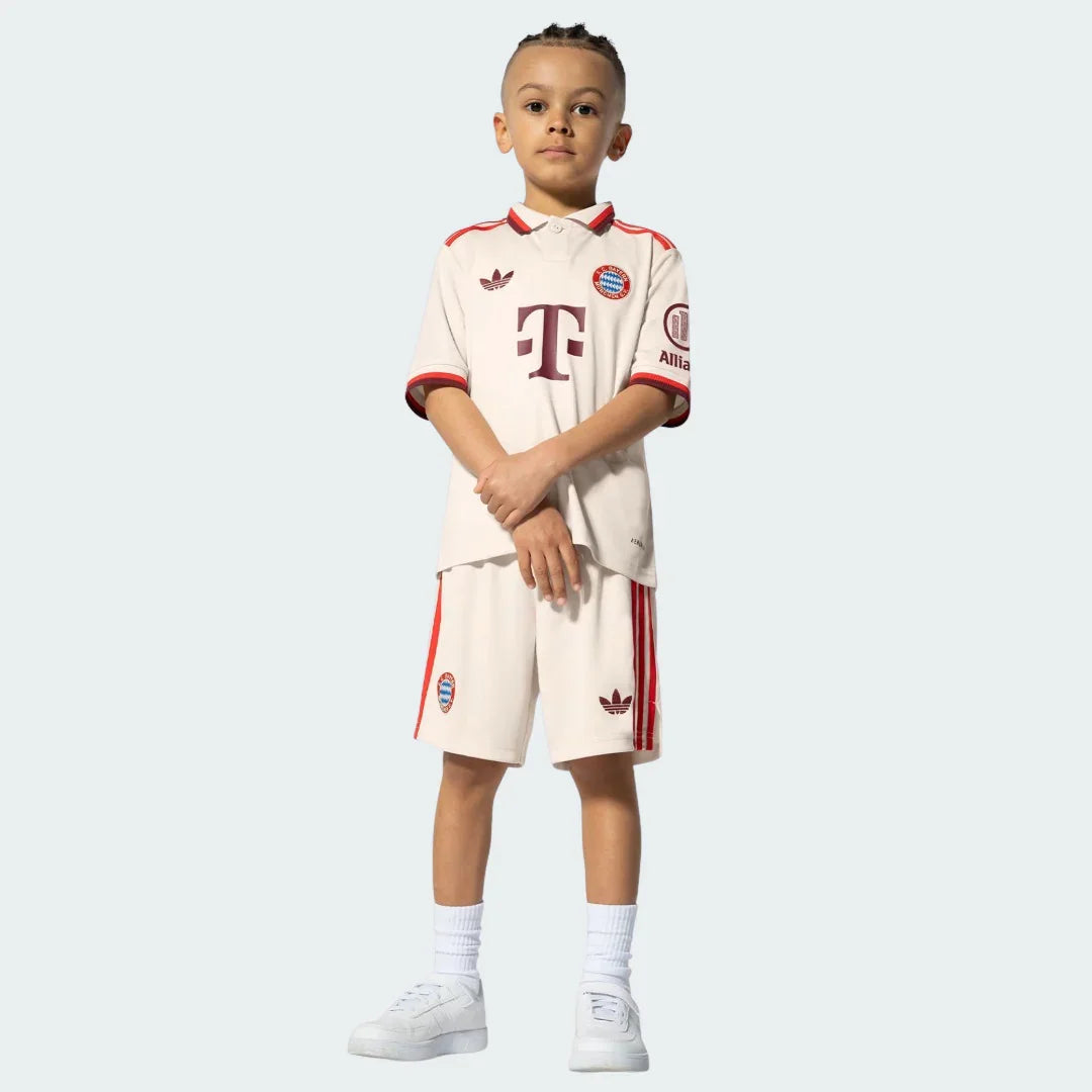 Criança usa o Kit Infantil Bayern de Munique III 24/25. Camisa e shorts na cor creme com detalhes em vermelho escuro.