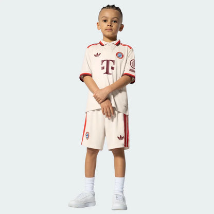 Criança usa o Kit Infantil Bayern de Munique III 24/25. Camisa e shorts na cor creme com detalhes em vermelho escuro.