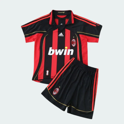 Foto de um kit infantil retrô Milan, camisa listrada vermelha e preta, shorts pretos, com escudos e patrocínio bwin.