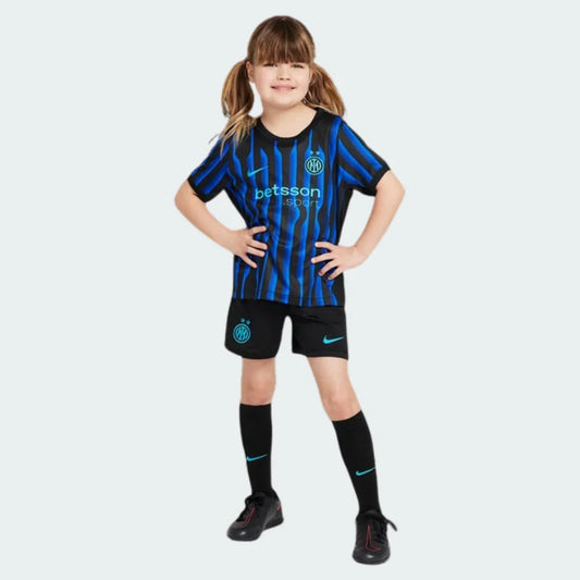 Menina sorridente veste kit infantil da Inter de Milão preto com listras azuis, shorts pretos e meias pretas em fundo branco.